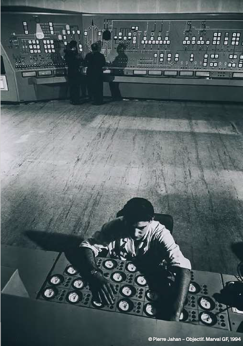 Lors de la mise en service du réacteur nucléaire G1 au CEA de Marcoule, des opérateurs sont photographiés dans   la salle de commande, aujourd'hui disparue. C'est d'ici que l'on pilote le réacteur à uranium naturel (non enrichi), modéré au graphite - d'où la lettre G - et refroidi à l'air atmosphérique. Après les installations de recherche du CEA Fontenayaux-Roses et de Saclay, le centre de production de plutonium de Marcoule", comprenant réacteurs et usines d'extraction du plutonium, marque l'entrée du CEA dans l'ère industrielle et militaire. Le réacteur Gl produit à la fois du plutonium destiné à la bombe nucléaire et aux futurs surgénérateurs, et les tout premiers kilowattheures d'électricité d'origine nucléaire. Il sera définitivement arrêté en 1968. (texte extrait de l'article de la Revue RGN numéro3 2025) © Pierre Jahan - Objectif, Marval GF, 1994